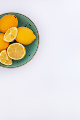 Fresh whole and cut lemons in a ceramic plate on a white table. Minimal citrus background for food, design or natural lifestyle themes.