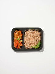 Buckwheat porridge with vegetable stew in a black container on a white background, healthy diet