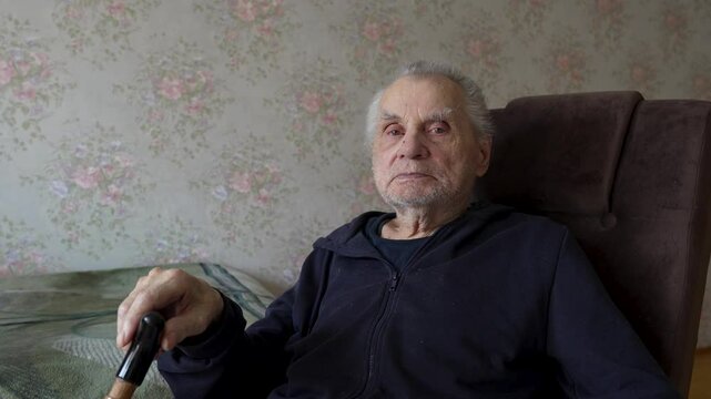 Elderly Man sitting in armchair looking at camera, holding cane