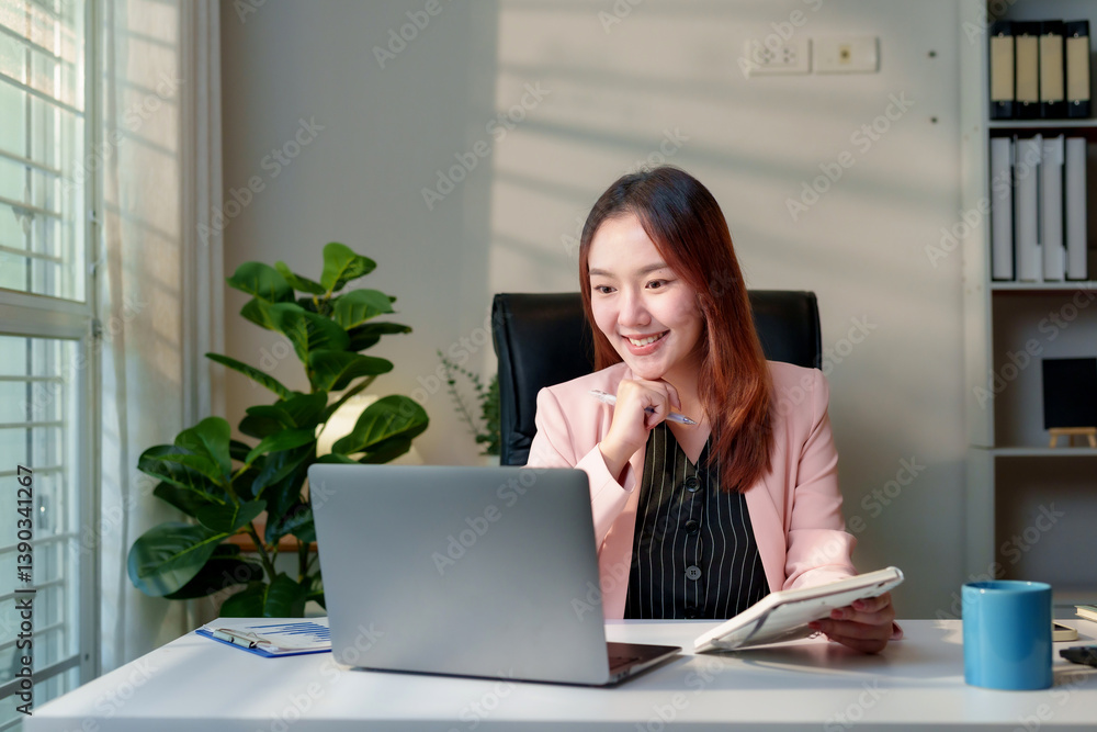 Poster asian businesswoman working from home using laptop computer and taking notes on a notebook, smiling 