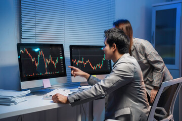 Two stockbrokers pointing at computer screens showing candlestick charts, analyzing cryptocurrency and financial market data