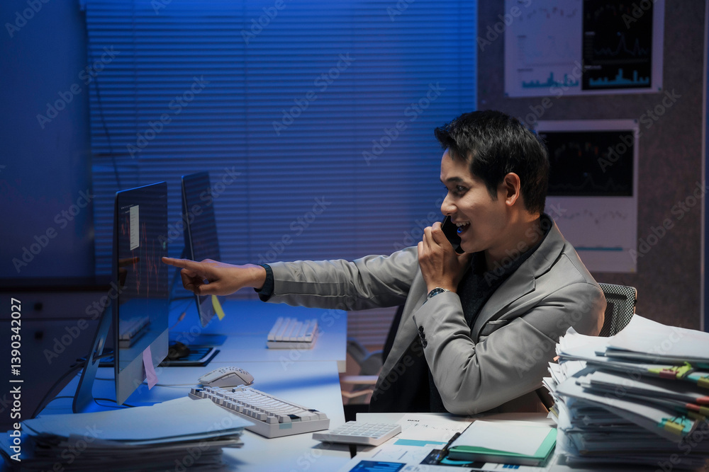 Poster young businessman pointing at computer monitor explaining something to a client on the phone, workin