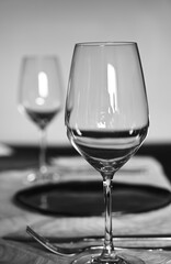 A refined black and white photograph of a table set for a formal meal, focusing on a clear wine glass in the foreground