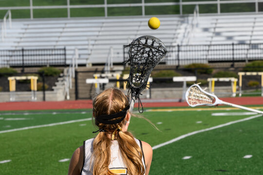 Girls on the JV Lacrosse Team practice throwing and catching on the sideline before the start of today's game. Girl with long hair tosses ball to her teammate.