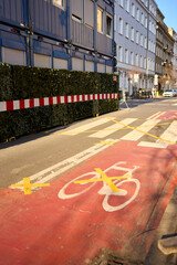 A red bike lane marked with yellow X tape, signaling closure or restriction. Urban textures, cracked asphalt, and morning light tell a silent story of change and interruption.