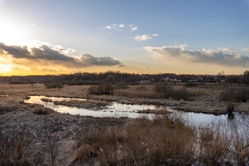 A field with a river running through it and a cloudy sky in the background