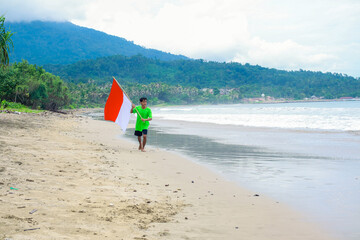 Young Man running with the Indonesian flag on the beach celebrating independence day
