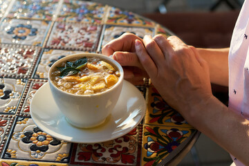 A warm citrus drink sits on a colorful mosaic table beside resting hands