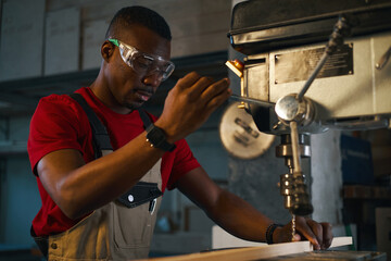 African American worker working on lathe with wooden plank in factory