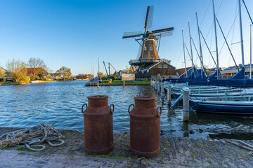 Naklejka premium Typical dutch scenery with two vintage rusty milk cans and the historical windmill in the village of Woudsend in Province of Friesland