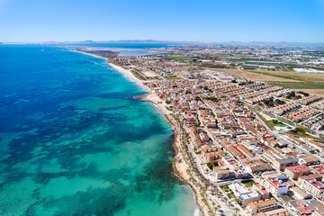 Fototapeta premium Aerial view coastal spanish town of Torre de la Horadada with houses rooftops, turquoise bay of Mediterranean Sea and sandy beach during sunny day. Costa Blanca, Alicante province. Spain