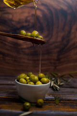 Cuchara con aceitunas, cayendo aceite sobre bol lleno de aceitunas