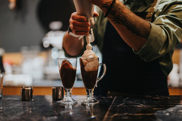 A barista decorates hot chocolate drinks with whipped cream in a cozy cafe setting.