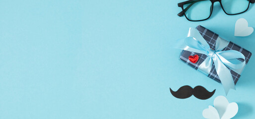 Happy Father's Day background. Stylish composition for Father's Day celebration with beautifully decorated gift with decorative mustache, paper hearts and glasses on light blue background.