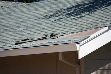 Asphalt shingle roofing on a residential home with visible damage, curled edges, and exposed sheathing. Close up.