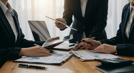 A focused team of business professionals collaborates on financial reports, analyzing data with tablets and charts in a modern office setting with soft light.