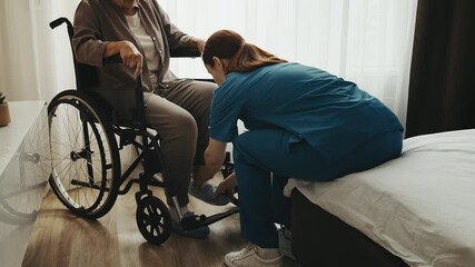 Caring medical worker assisting senior woman with disability in wheelchair, help