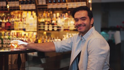 Smiling smart man drinking cocktail in Old fashioned with enjoy dancing in cheers with friends or stranger special vibrant beverage at nightclub on Friday meeting at luxurious counter bar. Vinosity.
