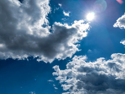 Bright sun shining through dramatic dark clouds in a vivid blue sky with intense light and contrast