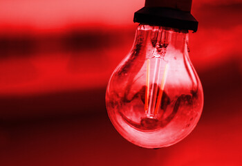 Red glass bulb with socket on an red black background. Abstract concept image of colorful light lamp glowing against orange tones. innovation, technology, futuristic concept. Copy space
