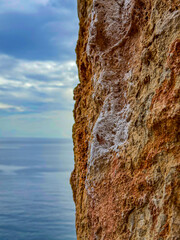 CLOSE UP, DOF: Detailed view of a textured limestone wall bearing white chalk marks left by climbers. Backdrop of sea and sky adds serenity and a nice color contrast to the rugged face of the rock.