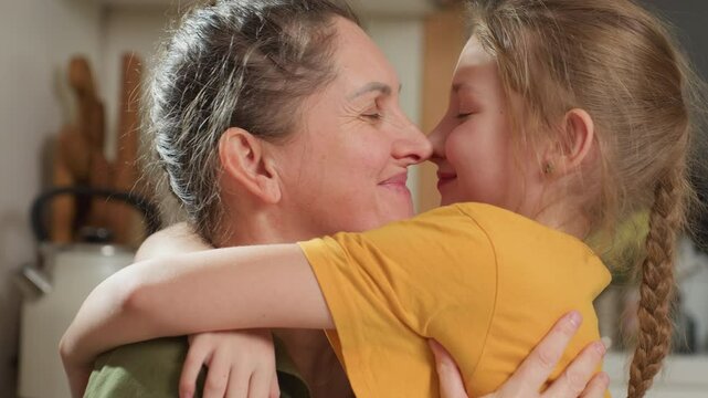 Joyful mother and daughter affectionately embrace in warm kitchen setting, smiling with eyes closed while playfully rubbing noses, expressing deep love, trust, and bonding