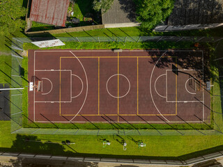 Obraz premium Aerial top down view of an outdoor basketball sports court of Haapsalu Primary School. The court is surrounded by a wire fence, green grass, and some gym equipment. Estonia