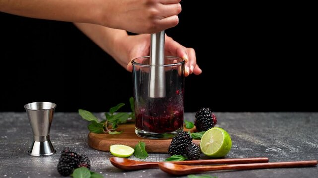 Preparing a blackberry mojito, mashing blackberries with a muddler to prepare a mojito