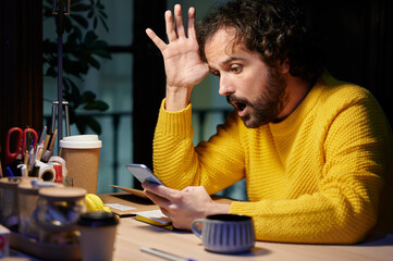 Man with a gesture of astonishment while using the mobile in the office at night.
