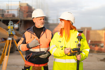 Male and female builders collaborate on-site, discussing project details while surveying at...