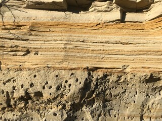 Close-up of layered sandstone showing horizontal striations and varying shades of tan, brown, and...