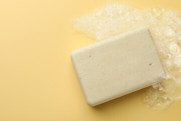 Soap bar with foam on yellow background, top view. Space for text
