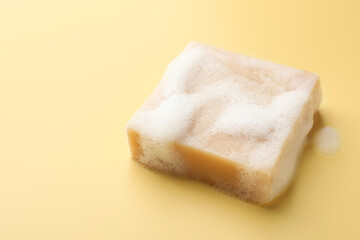 Soap bar with foam on yellow background, closeup. Space for text