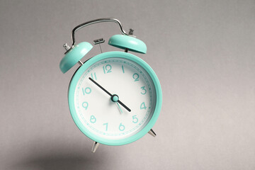 Turquoise alarm clock in air on light grey background