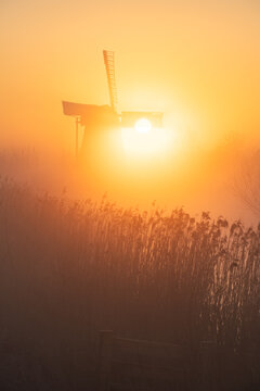 Sunrise at a Dutch, traditional windmill and a canal in the spring fog.