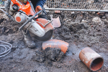 Builder using power saw to cut clay drainage pipe