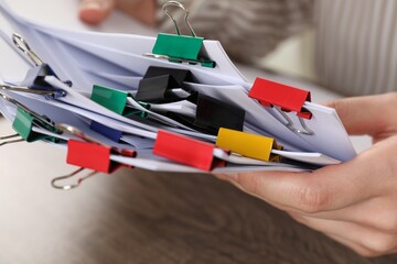Woman holding sheets of paper with metal binder clips at table, closeup
