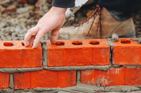Bricklaying process on construction site shows skilled worker placing red bricks with precision and care