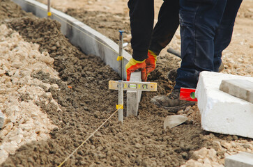 Builder checking level of  concrete edging curb at footway  construction