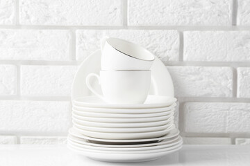Different clean dishware on white table near brick wall