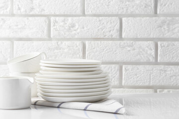 Different clean dishware on white table near brick wall. Space for text