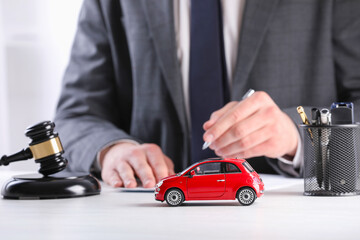 Auto accident law. Man working at table indoors, focus on toy car