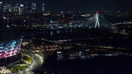 Nightfall in Warsaw as seen from above—PGE Narodowy, Świętokrzyski Bridge, and the city glowing in golden hues.