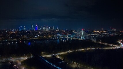Aerial view of Warsaw after dark, Świętokrzyski Bridge, and a vibrant cityscape.