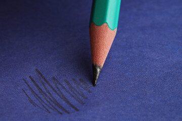 Drawing strokes with graphite pencil on blue background, closeup