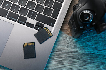SD memory cards, camera and laptop on wooden table, flat lay