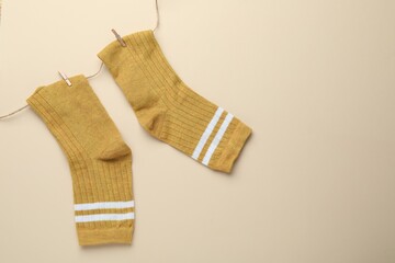 Pair of soft socks, clothespins and rope on beige background, top view. Space for text