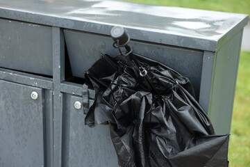 Broken black umbrella in garbage bin outdoors
