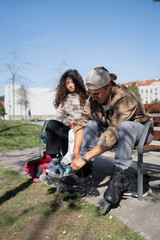 Father tying inline skates while daughter waits on park bench