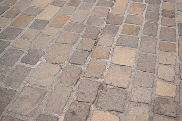 Old stone pavement with beige and brown cobblestones in a historic European city. Weathered texture background for architecture and travel concepts.
